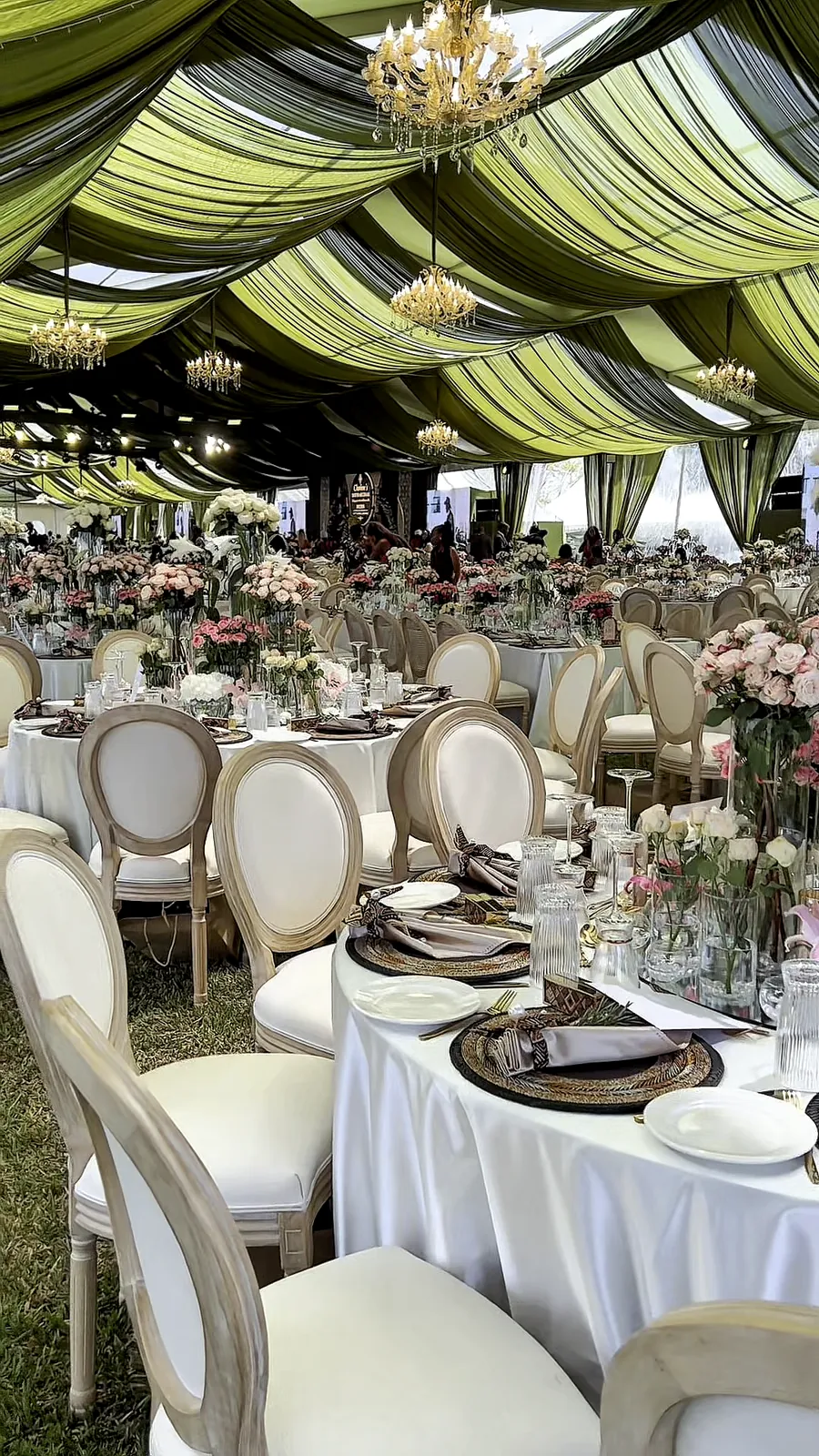 Guest tables with white chairs and flower centrepieces across the marquee