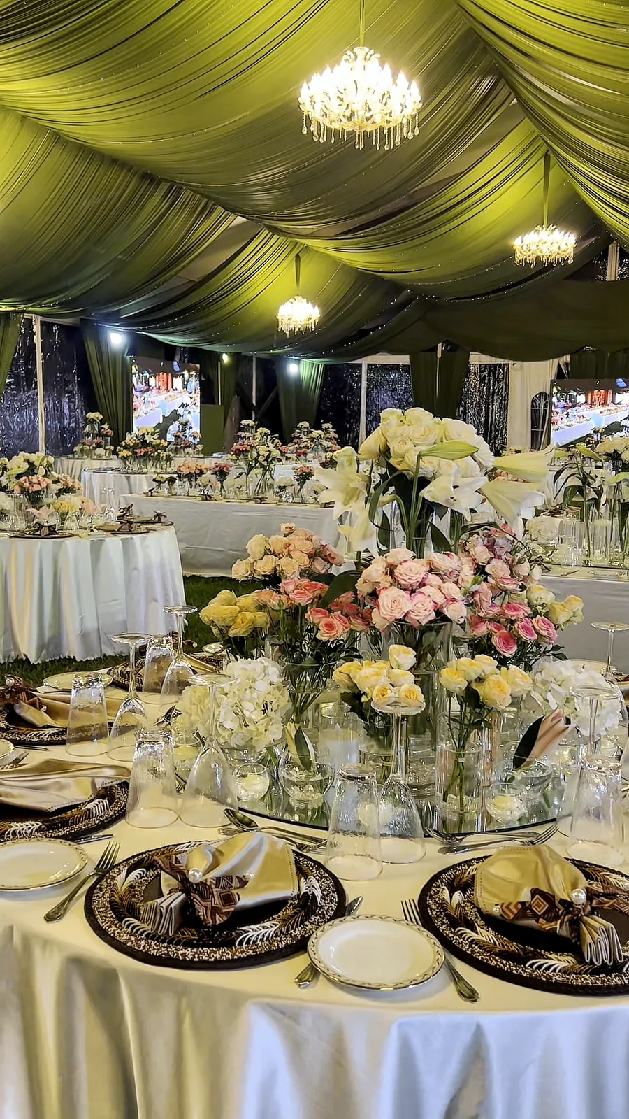 A round table set with chrysanthemums, roses and lilies in glass vases beneath a chandelier