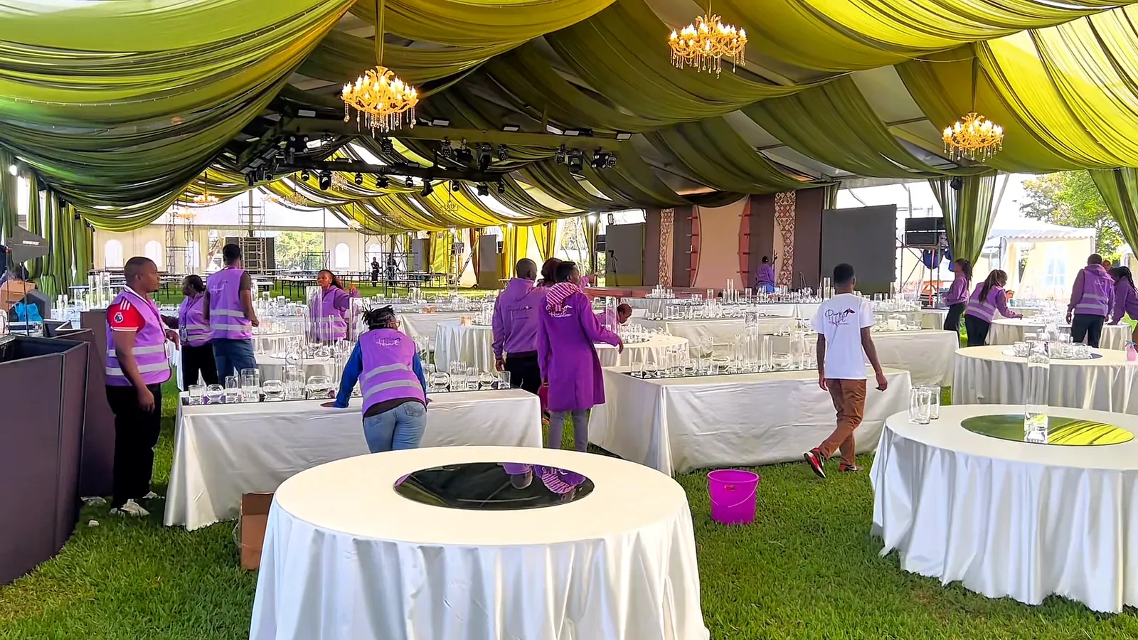The Purple Heart team preparing round tables inside a green-draped marquee