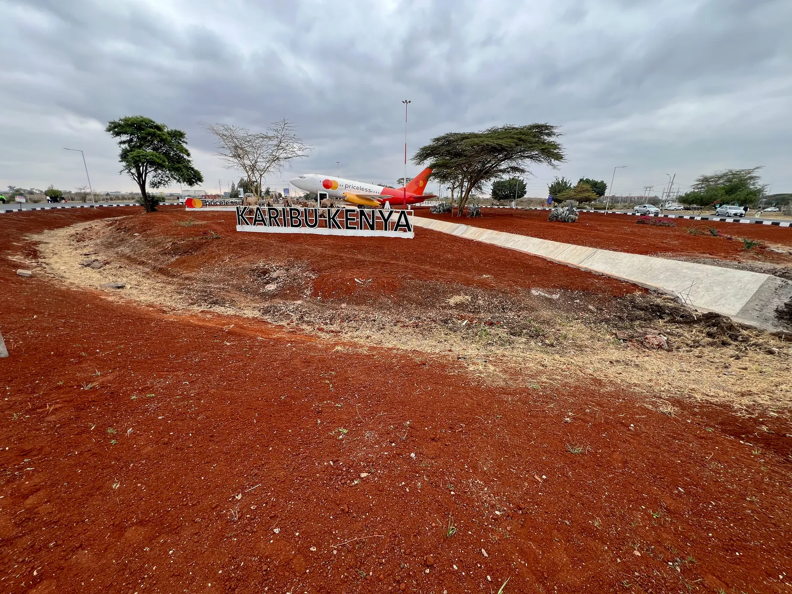 The JKIA approach before planting: shaped red-soil beds around the Karibu Kenya sign